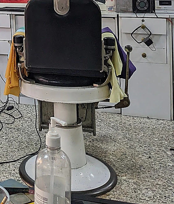 Sillón de peluquería de base blanca y respaldo de piel negra, vacío, sobre el piso de granito