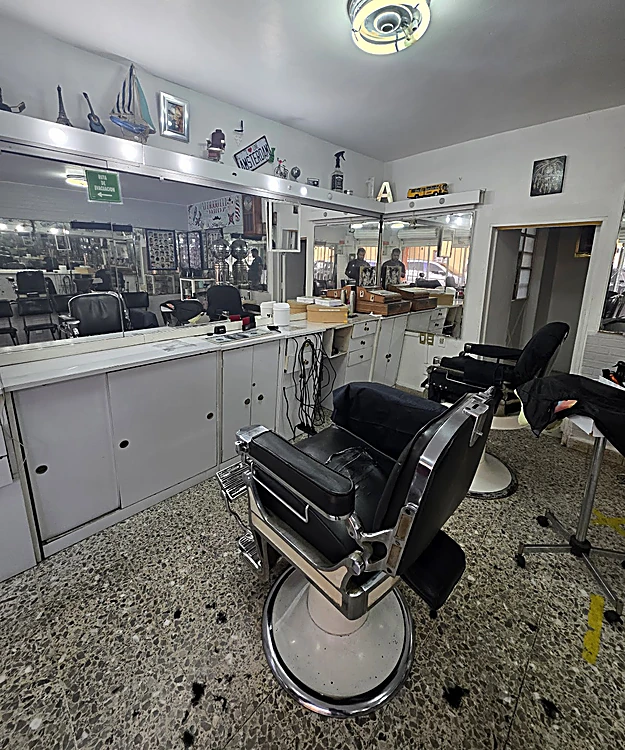 Sillón de peluquería de cromo y piel negra con base blanca frente a los espejos y gabinetes del salón