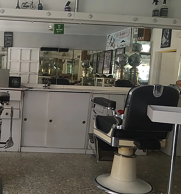 Sillón de peluquería negro y cromado frente a un mueble blanco; en el espejo se reflejan dos esterilizadores cromados